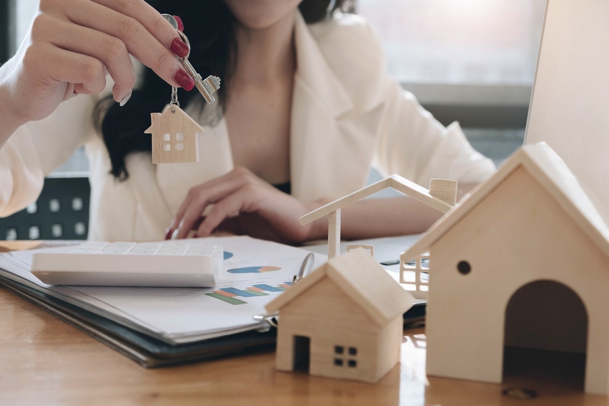 recorte asesora inmobiliaria en despacho mostrando llave de vivienda con casas de madera en miniatura sobre la mesa